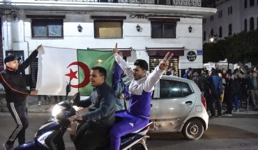 An Algerian flashes the victory gesture while seated on a scooter as another two hold a national flag behind him during a demonstration in the centre of the capital Algiers on March 11, 2019, after President Abdelaziz Bouteflika announced his withdrawal from a bid to win another term in office and postponed an April 18 election, following weeks of protests against his candidacy.
