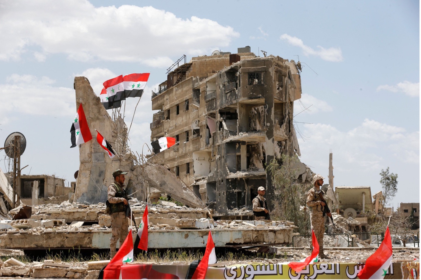 Image 8: Regime forces attend a flag raising ceremony at the entrance of Al-Hajar al-Aswad neighborhood, May 24, 2018. Photo by Louai Beshara/AFP via Getty Images