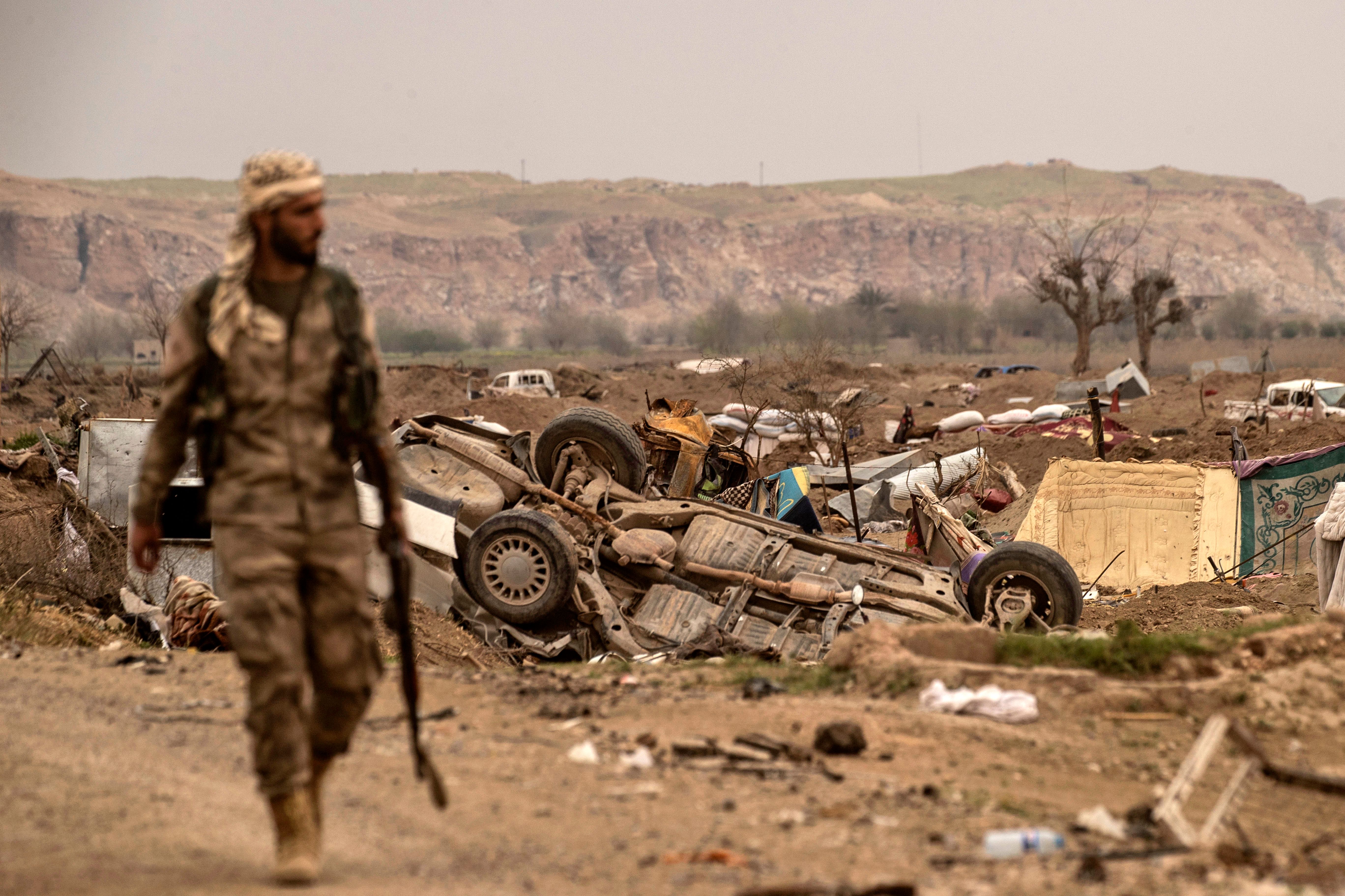 A member of the SDF walks past damaged vehicles on the side of a road in the village of Baghouz in Syria's eastern Deir ez-Zor Province on March 24, 2019, a day after the ISIS "caliphate" was declared defeated. Photo by DELIL SOULEIMAN/AFP via Getty Images.