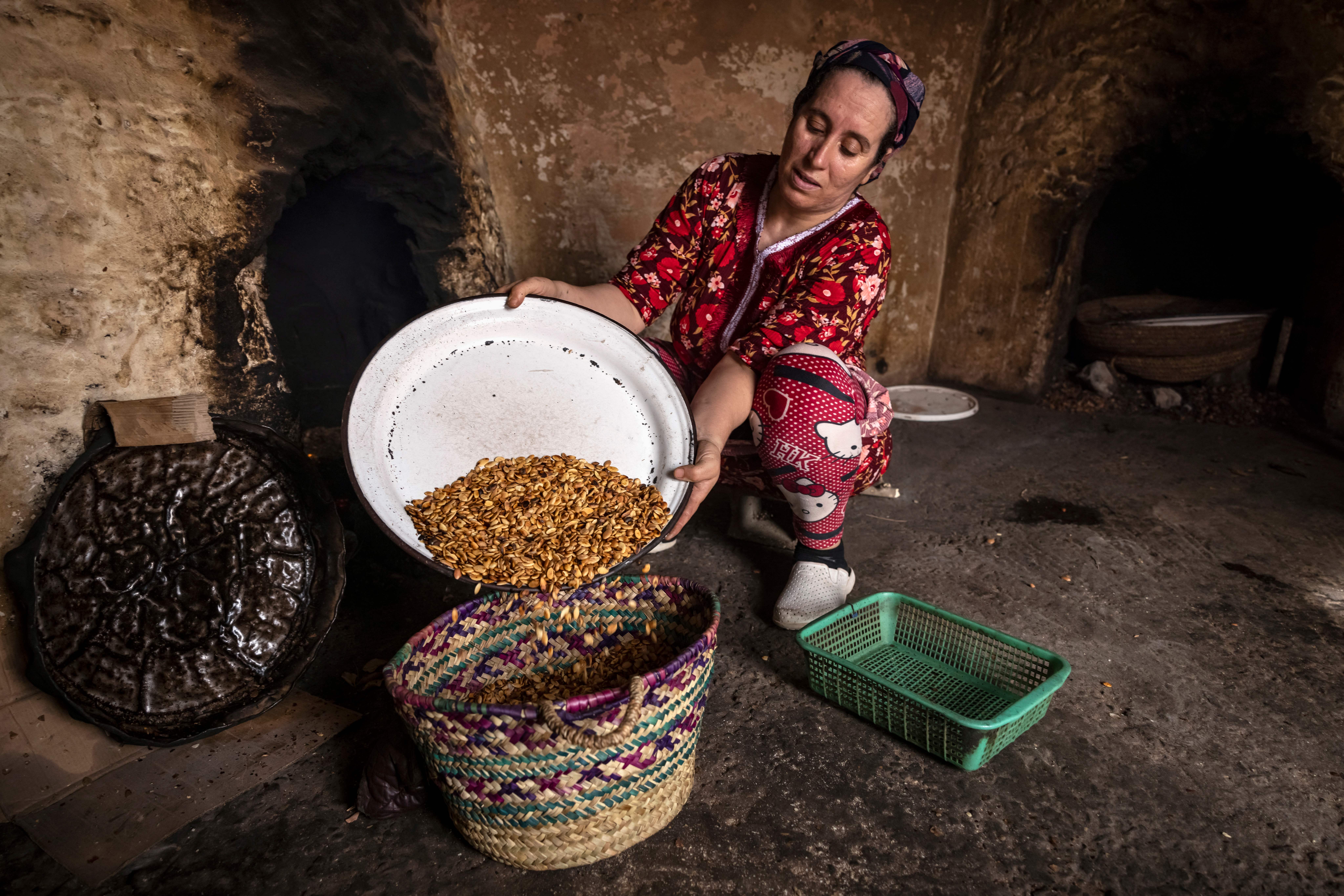 A woman empties roasted argan nuts into a basket as she makes oil at her home near Essaouira, Morocco, on Oct. 15, 2022. Photo by FADEL SENNA/AFP via Getty Images.