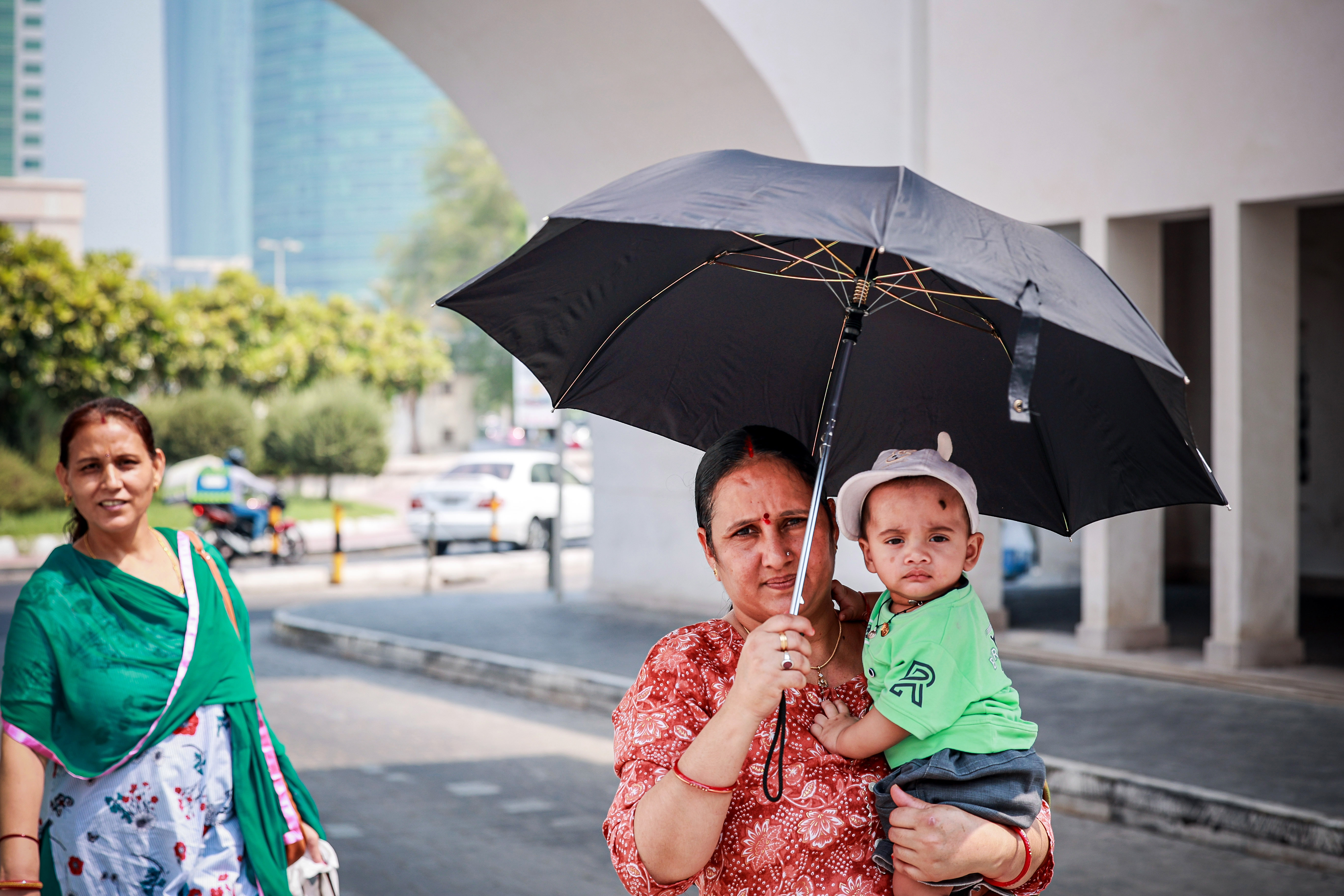 A woman protects her child with an umbrella in Manama as scorching heat and humidity affect the Gulf countries on Aug. 21, 2023. Photo by Ayman Yaqoob/Anadolu Agency via Getty Images.