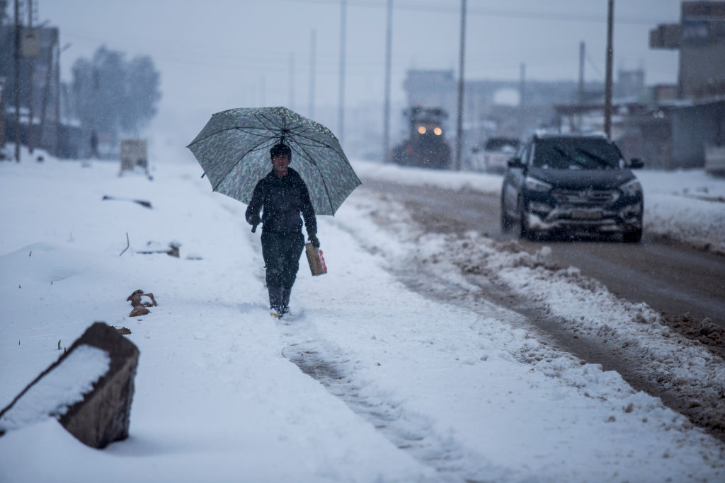 A young guy with his umbrella walking close to the street with a gallon to get fuel for heating with the snow weather. Photo by BaderKhan Ahmad/Barcroft Media via Getty Images)