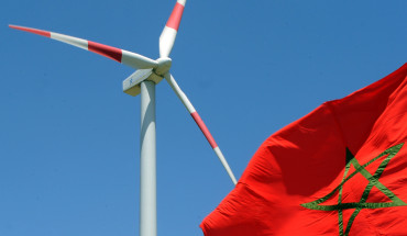 A Moroccan flag flies next to a wind turbine on June 28, 2010, at a wind farm near Tangiers shortly after its inauguration by Moroccan King Mohammed VI. Photo by ABDELHAK SENNA/AFP via Getty Images.