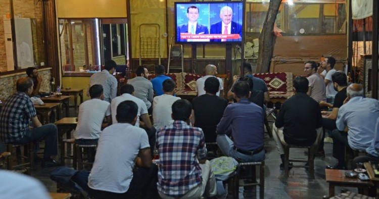 People watch a live broadcast of a televised debate between Istanbul's mayoral candidate Binali Yildirim (R) of Turkey's ruling AKP, and Istanbul's deposed mayor Ekrem Imamoglu (L) of the CHP, is shown on a screen at a tea house in Diyarbakir on June 16, 2019.