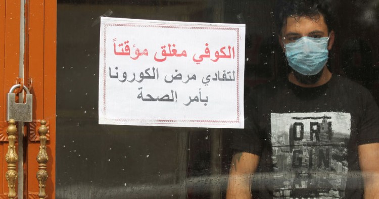 An Iraqi man, wearing a protective mask, stands inside a coffee shop with a sign in Arabic which reads "Coffee shop is closed, due to corona following a decision by the Health ministry" in the capital Baghdad on March 16, 2020 amidst efforts against the spread of COVID-19 coronavirus disease. 