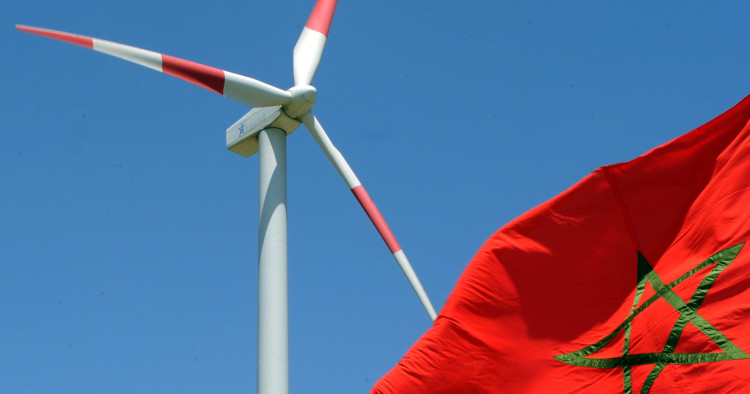 A Moroccan flag flies next to a wind turbine on June 28, 2010, at a wind farm near Tangiers shortly after its inauguration by Moroccan King Mohammed VI. Photo by ABDELHAK SENNA/AFP via Getty Images.