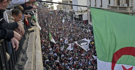 Algerians wave a national flag from a balcony as they watch anti-government demonstrators march in the capital Algiers on December 6, 2019, ahead of the presidential vote scheduled for December 12.