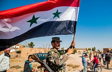  A Syrian regime soldier waves the national flag a street on the western entrance of the town of Tal Tamr in the countryside of Syria's northeastern Hasakeh province on October 14, 2019. 