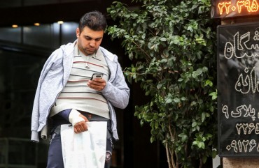 A man looks at a smartphone in his hand while walking outside along a street in the Iranian capital Tehran on November 17, 2019. - Iran's supreme leader on November 17 threw his support behind a decision to hike petrol prices, a move that sparked nationwide unrest in which he said "some lost their lives". Access to the internet has been restricted since demonstrations broke out two days prior, after a decision by the Supreme National Security Council of Iran.