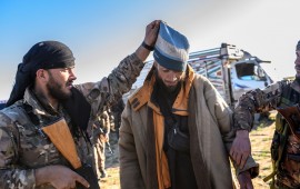 A member of the SDF raises the hood of a Bosnian man suspected of being an ISIS fighter as he is searched after leaving the group’s last holdout of Baghouz, on March 1, 2019.