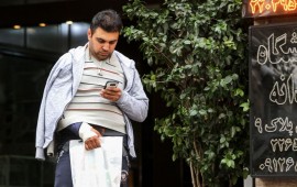 A man looks at a smartphone in his hand while walking outside along a street in the Iranian capital Tehran on November 17, 2019. - Iran's supreme leader on November 17 threw his support behind a decision to hike petrol prices, a move that sparked nationwide unrest in which he said "some lost their lives". Access to the internet has been restricted since demonstrations broke out two days prior, after a decision by the Supreme National Security Council of Iran.