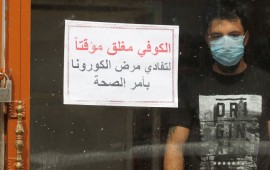 An Iraqi man, wearing a protective mask, stands inside a coffee shop with a sign in Arabic which reads "Coffee shop is closed, due to corona following a decision by the Health ministry" in the capital Baghdad on March 16, 2020 amidst efforts against the spread of COVID-19 coronavirus disease. 