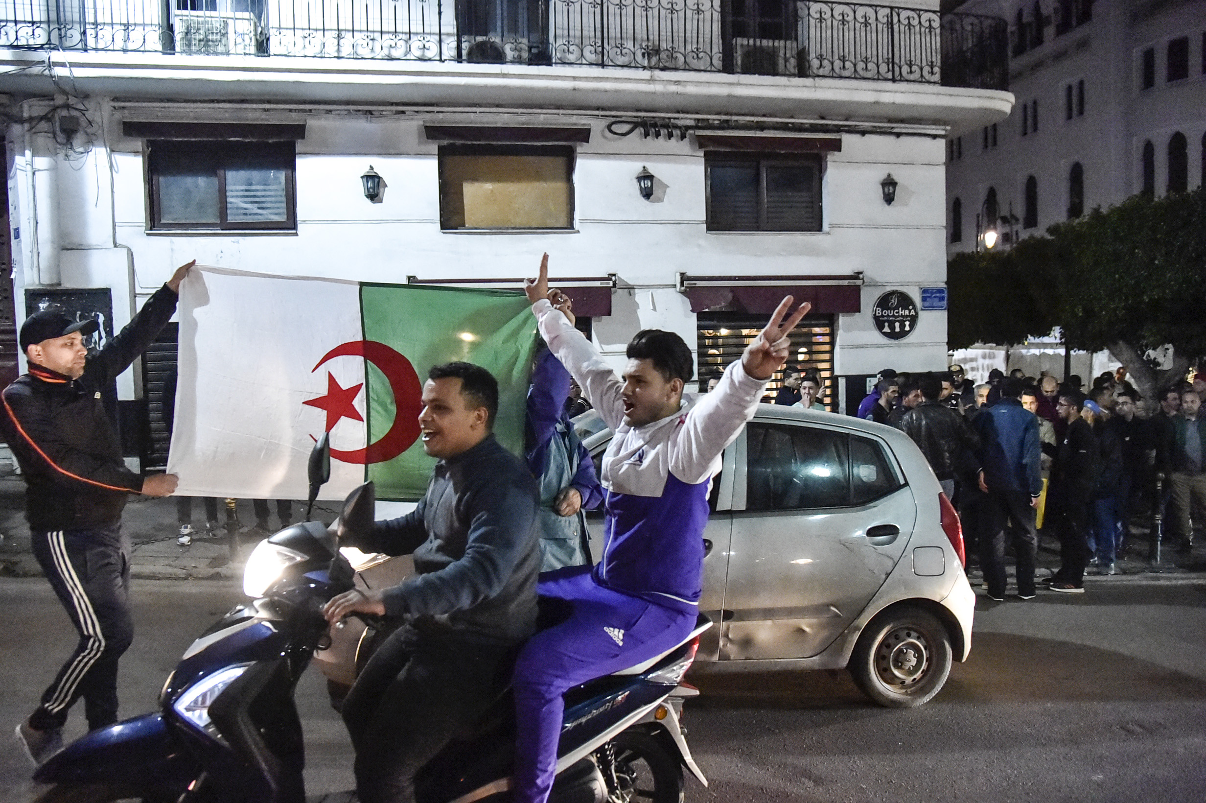 An Algerian flashes the victory gesture while seated on a scooter as another two hold a national flag behind him during a demonstration in the centre of the capital Algiers on March 11, 2019, after President Abdelaziz Bouteflika announced his withdrawal from a bid to win another term in office and postponed an April 18 election, following weeks of protests against his candidacy.