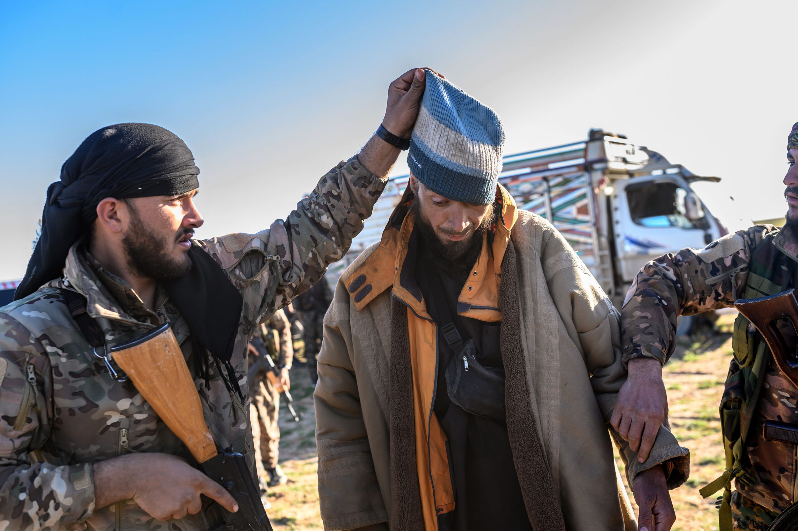 A member of the SDF raises the hood of a Bosnian man suspected of being an ISIS fighter as he is searched after leaving the group’s last holdout of Baghouz, on March 1, 2019.