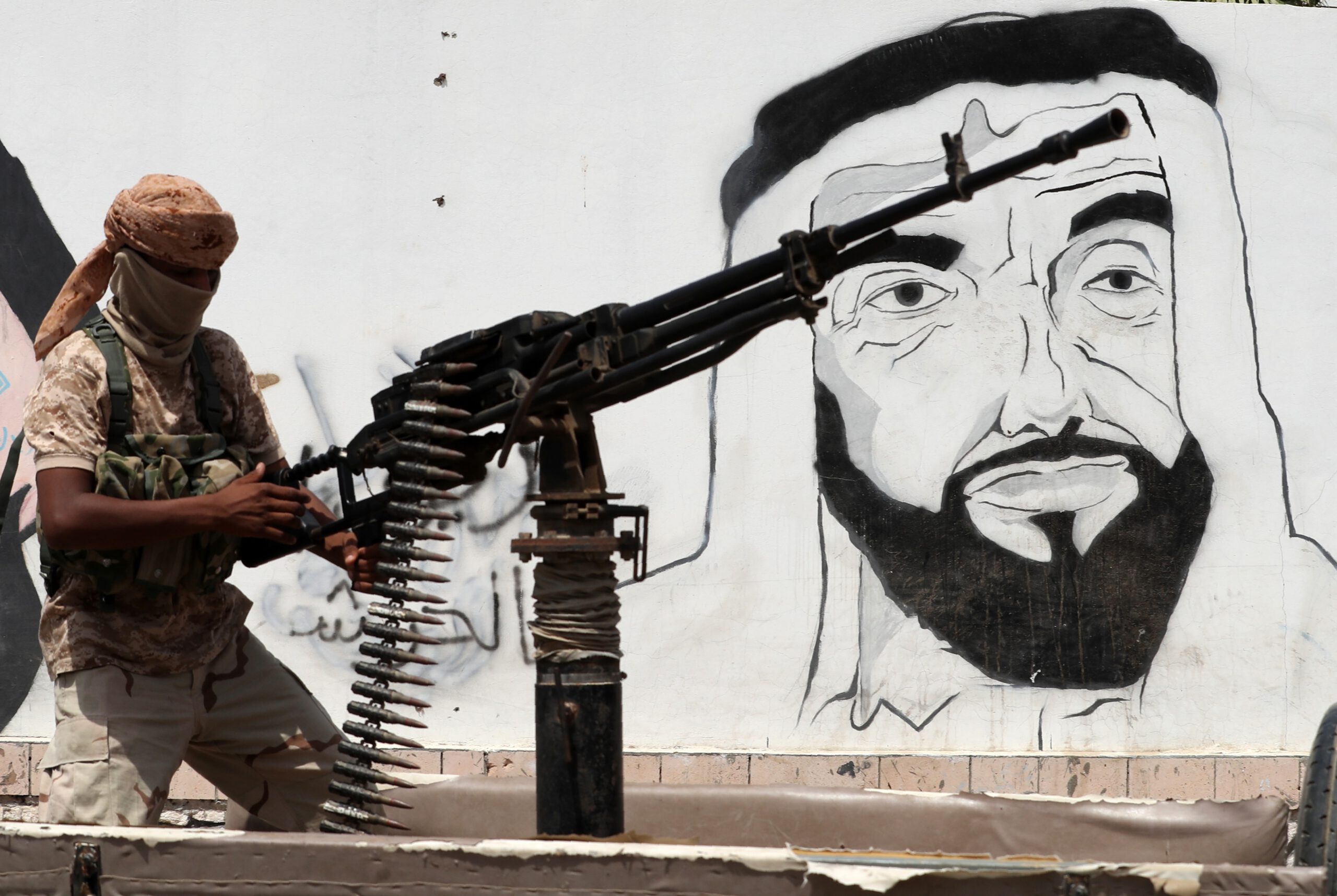A picture taken on August 8, 2018 during a trip in Yemen organised by the UAE's National Media Council (NMC) shows a soldier loyal to the Saudi and UAE-backed government, manning a machine gun mounted on a vehicle passing by a mural depicting the late UAE founder and president Sheikh Zayed bin Sultan al-Nahyan, along a street in the southeastern port city of Mukalla, the capital of Hadramawt province. 