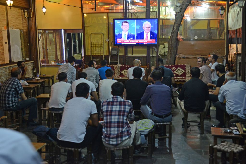 People watch a live broadcast of a televised debate between Istanbul's mayoral candidate Binali Yildirim (R) of Turkey's ruling AKP, and Istanbul's deposed mayor Ekrem Imamoglu (L) of the CHP, is shown on a screen at a tea house in Diyarbakir on June 16, 2019.