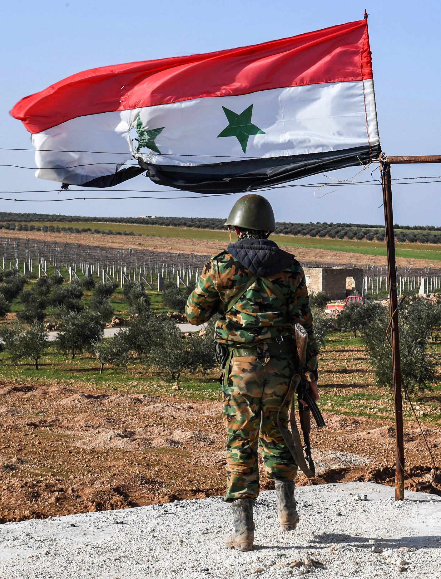 A Syrian soldier walks towards a fluttering Syrian flag on a roof at a government forces' position in the village of Hawshariya. Photo credit: GEORGE OURFALIAN/AFP/Getty Images.