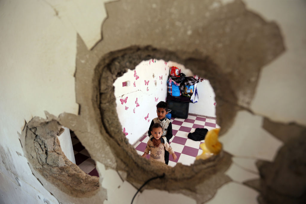 Displaced Yemeni children from the Hodeidah province are pictured on September 30, 2018 through a hole in a damaged house where they have been living with other displaced families in the southwestern Yemeni city of Taiz.