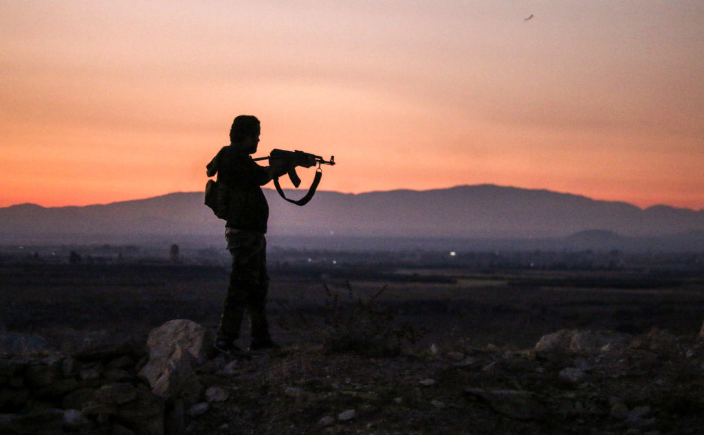 A Syrian rebel fighter aims his Kalashnikov assault rifle as he stands near the frontline against government forces west of the embattled southern city of Daraa on July 3, 2018. 