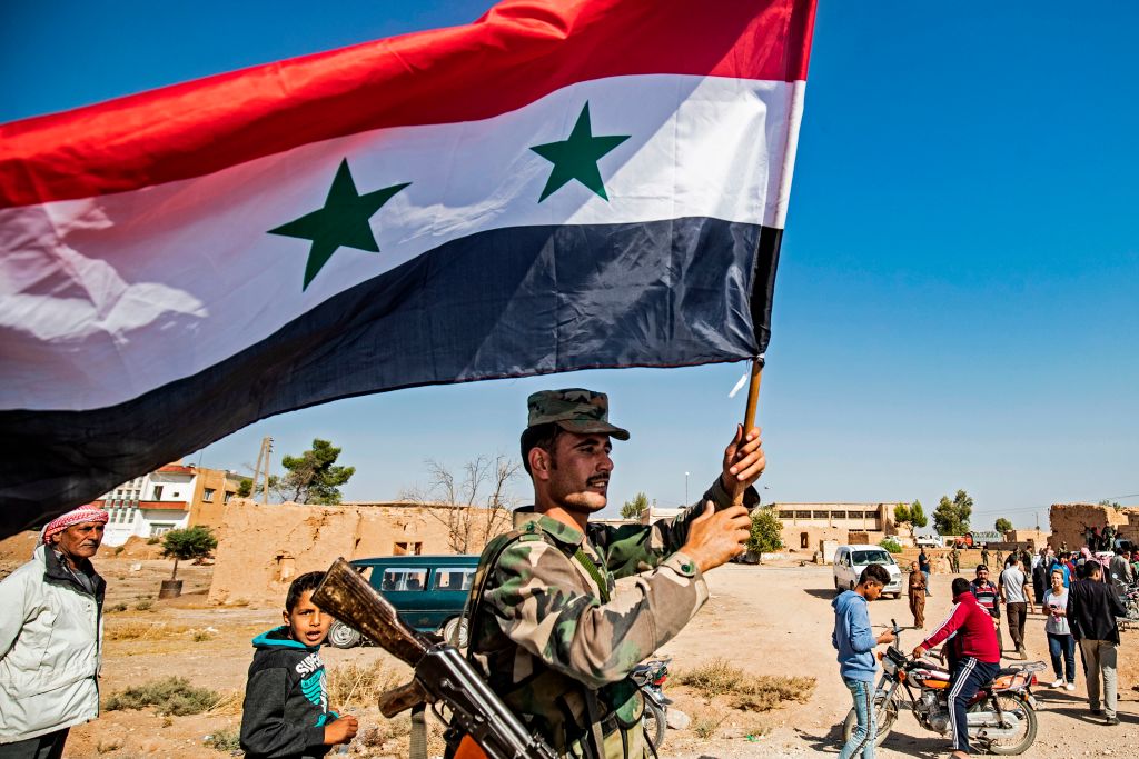 A Syrian regime soldier waves the national flag a street on the western entrance of the town of Tal Tamr in the countryside of Syria's northeastern Hasakeh province on October 14, 2019.