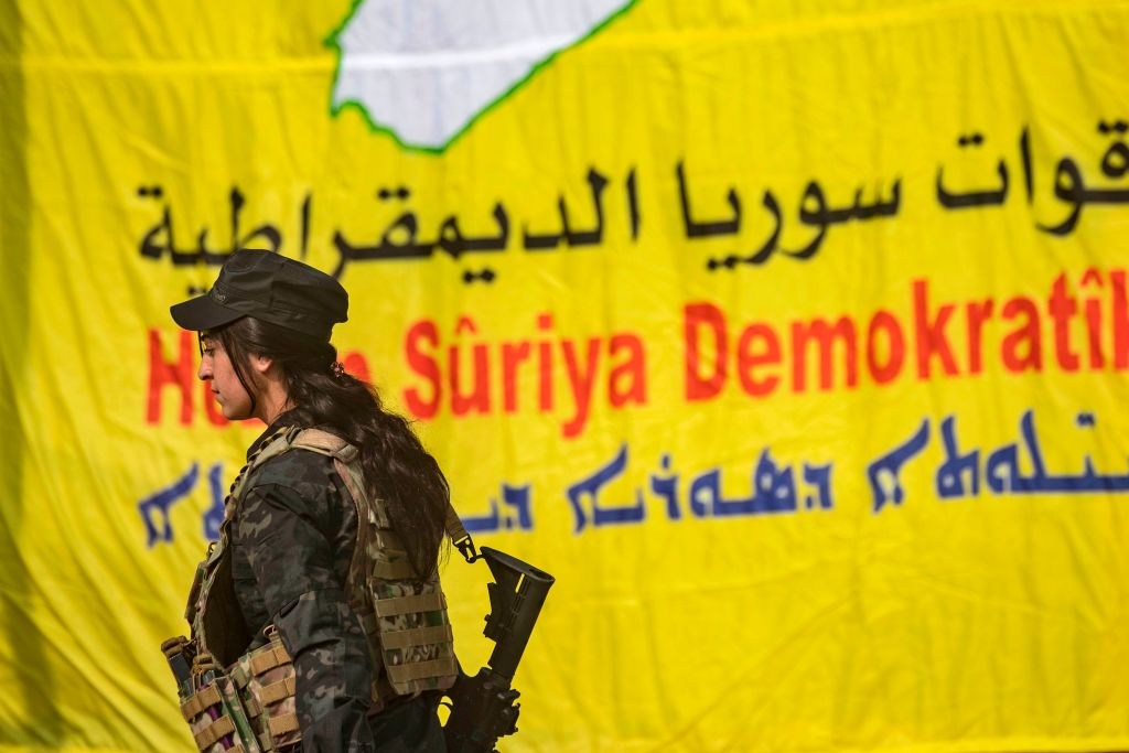 A fighter of the US-backed Kurdish-led SDF walks in front of a banner during celebrations near the Omar oil field in Deir Ezzor province on March 23, 2019, after announcing the total elimination of ISIS's last bastion in eastern Syria. 