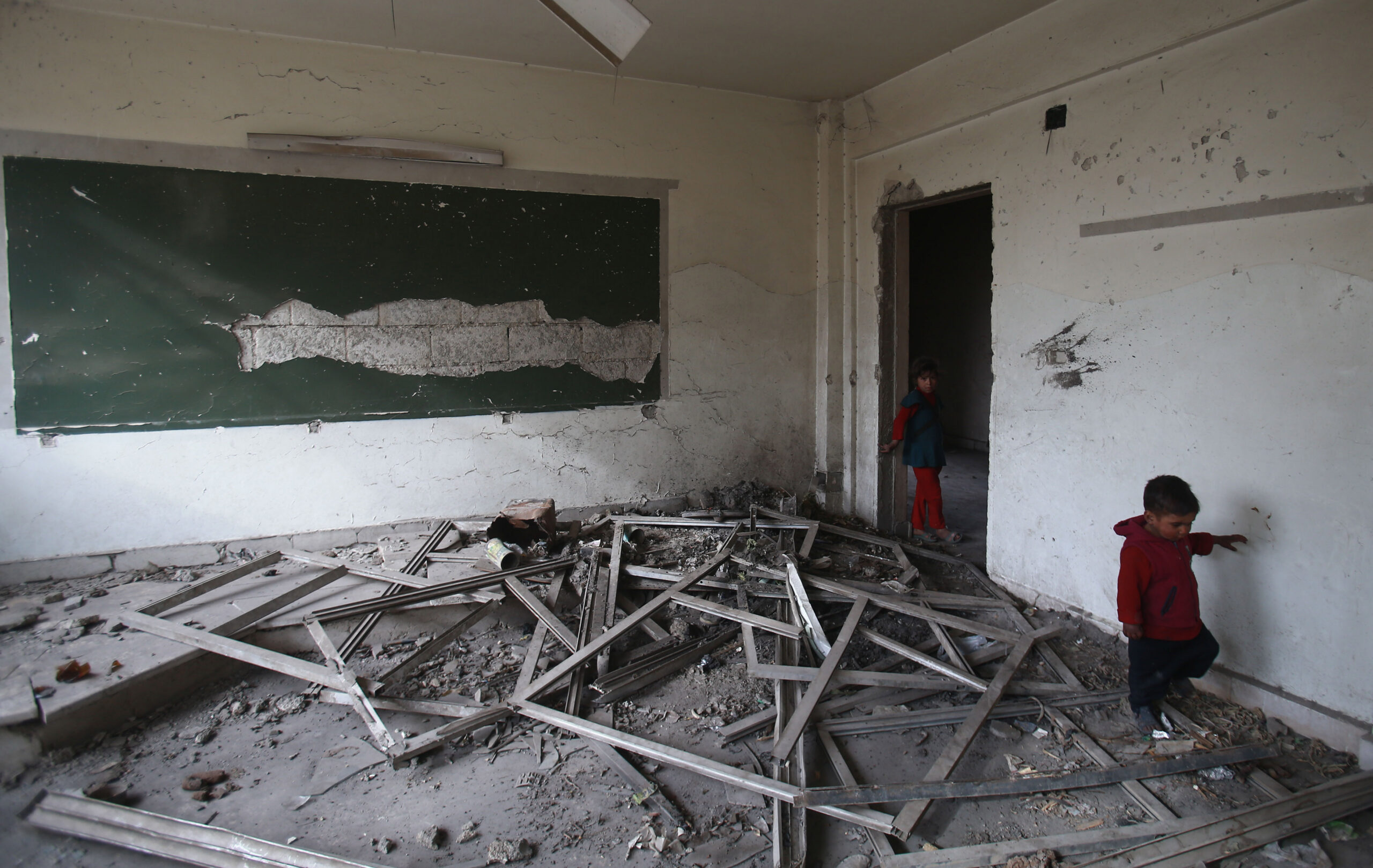 Syrian children walk in a heavily damaged classroom at a school turned into a shelter for people displaced by the war, in the rebel-controlled town of Hamouria, in the eastern Ghouta region on the outskirts of the capital Damascus on December 23, 2017. As