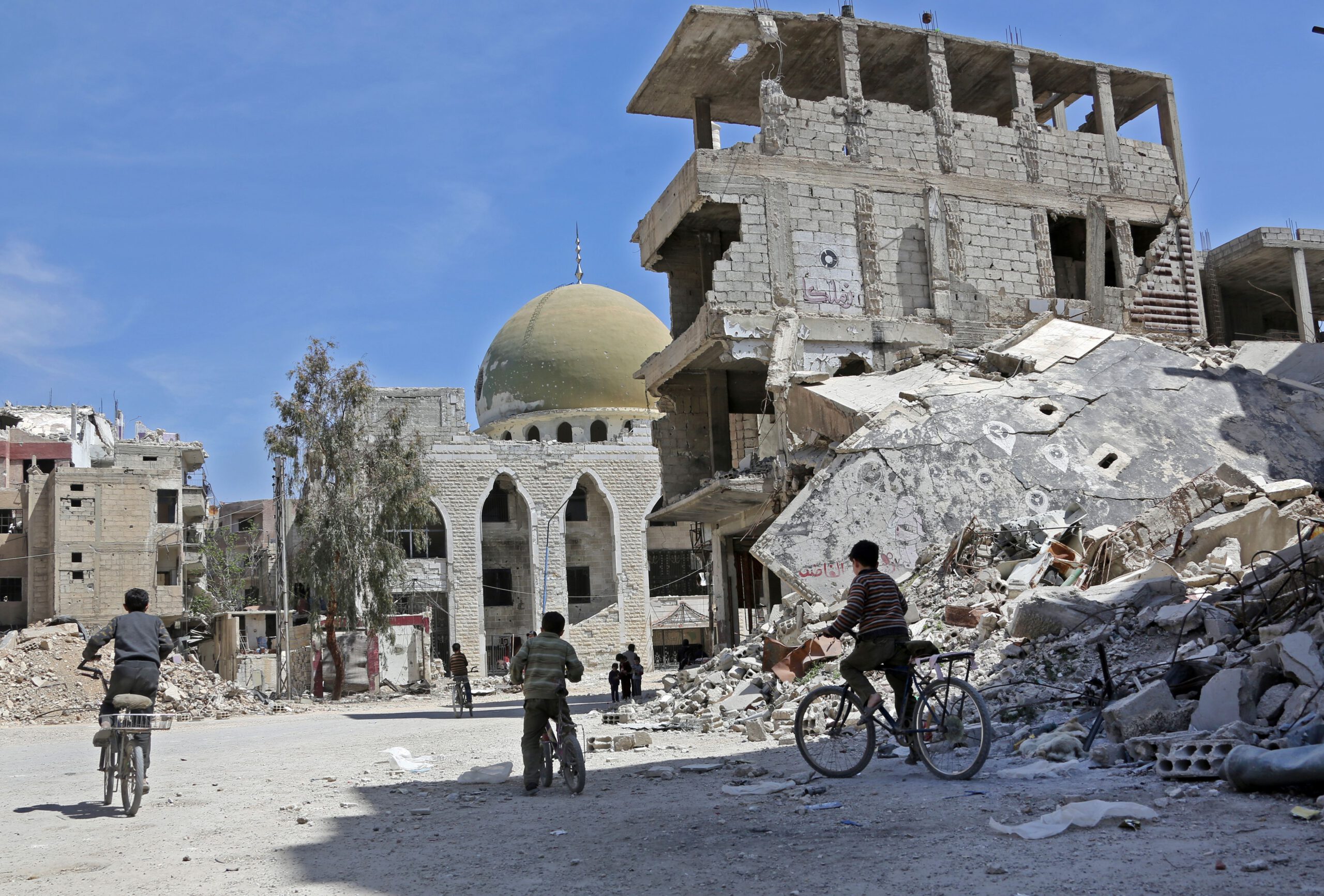 Syrian children ride their bike past destroyed buildings in the former rebel-held town of Zamalka, in Eastern Ghouta on April 5, 2018. / AFP PHOTO / STRINGER (Photo credit should read STRINGER/AFP via Getty Images)