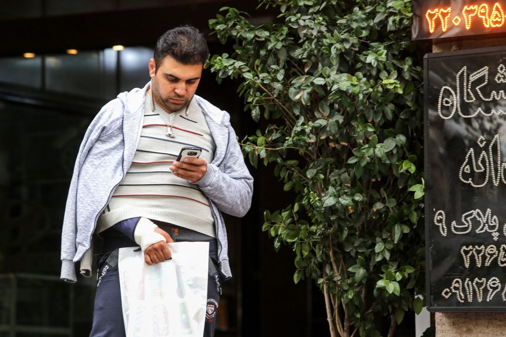 A man looks at a smartphone in his hand while walking outside along a street in the Iranian capital Tehran on November 17, 2019. - Iran's supreme leader on November 17 threw his support behind a decision to hike petrol prices, a move that sparked nationwide unrest in which he said 