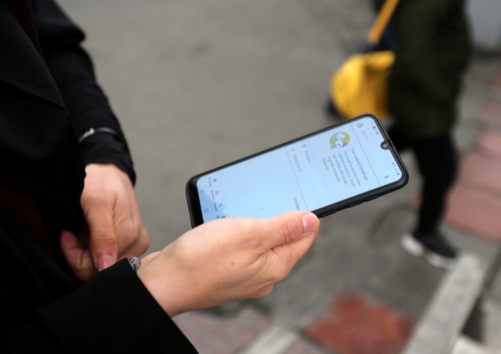 A woman holds a smartphone shown to be unable to access internet, while standing along a street in the Iranian capital Tehran on November 23, 2019. 