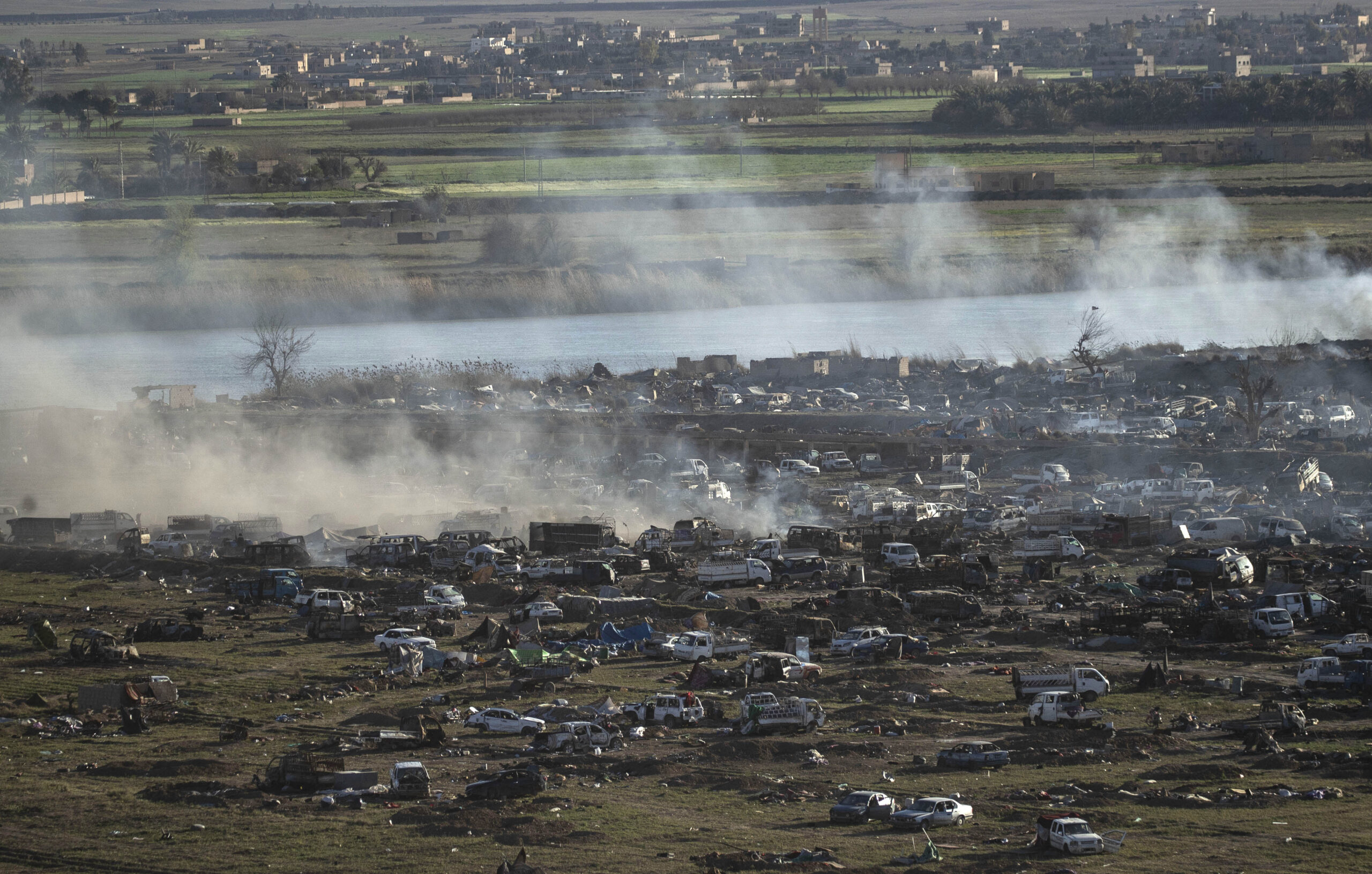 Smoke rises in the Islamic State (IS) group's last remaining position on the eastern banks of the Euphrates River (C) in the village of Baghouz during battles with the Syrian Democratic Forces (SDF), in the countryside of the eastern Syrian province of Deir Ezzor, on March 18, 2019. - An air strike pounds a demolished bridge in eastern Syria, sending armed men scampering to hide among the cars and tents of the Islamic State group's smouldering last redoubt. (Photo by Delil SOULEIMAN / AFP) (Photo credit sho
