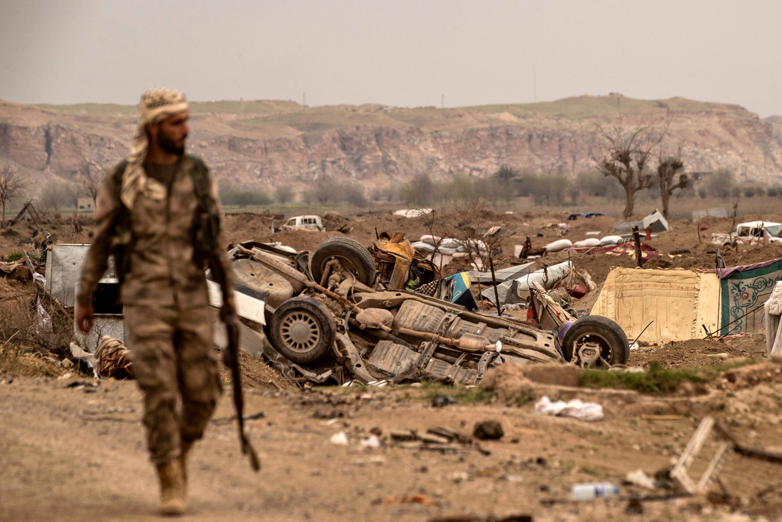 TOPSHOT - EDITORS NOTE: Graphic content / A member of the Syrian Democratic Forces (SDF) walks past damaged vehicles on the side of a road in the village of Baghouz in Syria's eastern Deir Ezzor province near the Iraqi border on March 24, 2019, a day after the Islamic State (IS) group's 