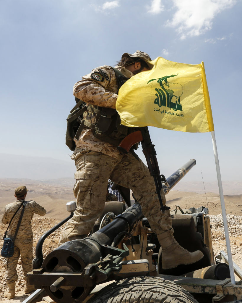 A picture taken on August 2, 2017 during a tour guided by the Lebanese Shiite Hezbollah movement shows one of the group's fighters stepping on an artillery gun with the group's flag flying by, in a mountainous area around the Syrian town of Flita near the border with Lebanon. / AFP PHOTO / LOUAI BESHARA (Photo credit should read LOUAI BESHARA/AFP via Getty Images)