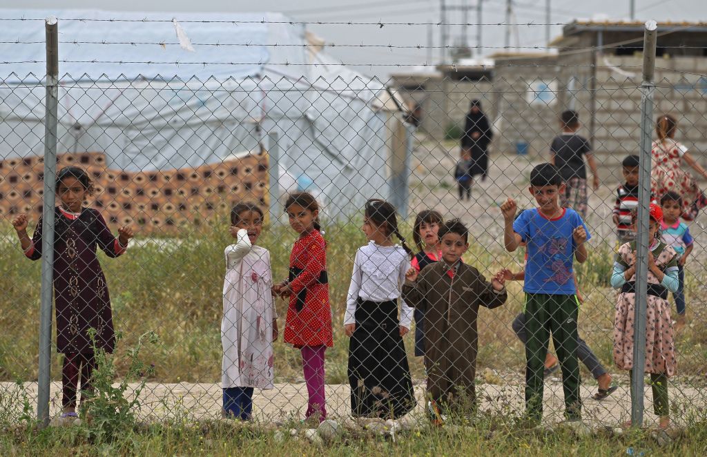Children stand behind a wire fence, at Laylan camp for the displaced about 25 kilometres east of the northern multi-ethnic Iraqi city of Kirkuk on May 9, 2019. - Residents of Laylan fled their hometowns in Hawija, Baiji and Salah al-Din during battles by the government to retake the areas seized by the Islamic State (IS) group in 2014. 