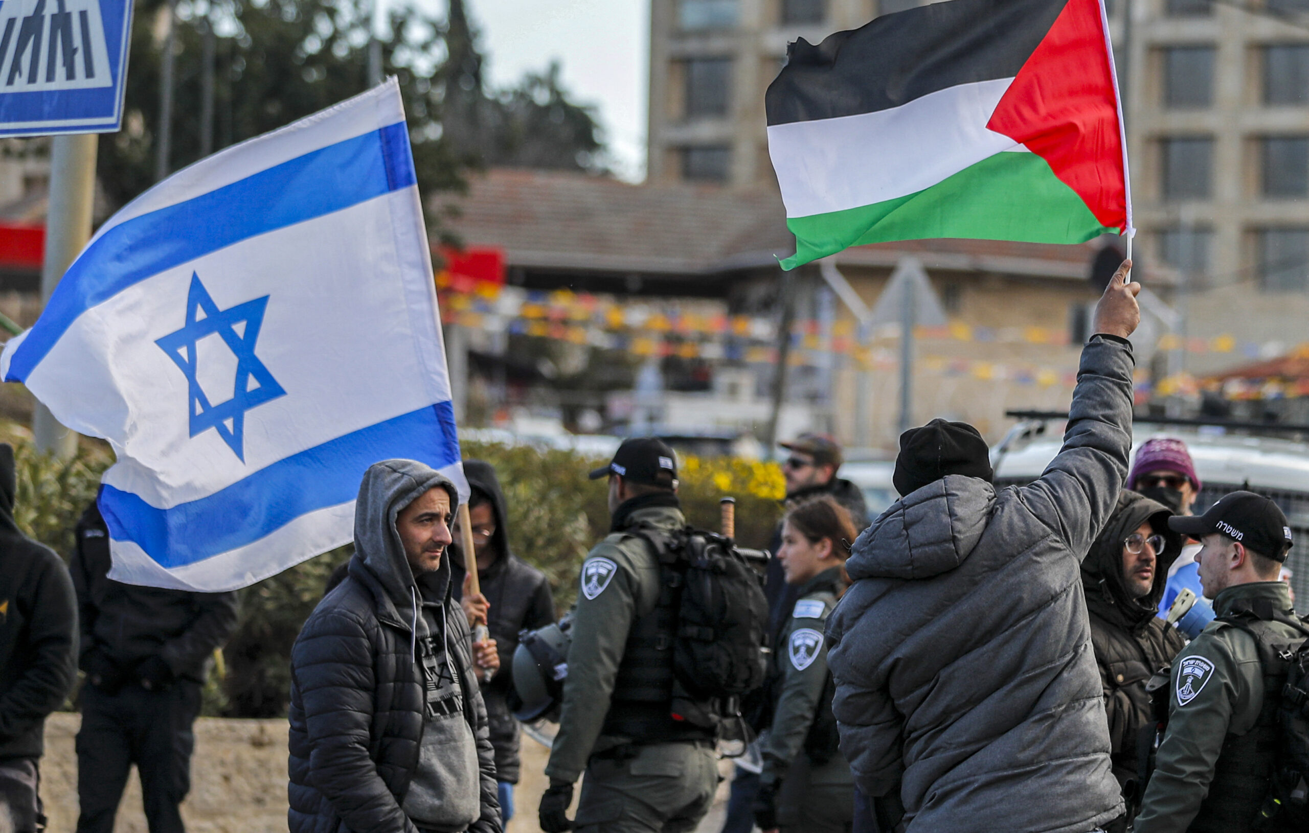 Photo above: An Israeli settler stands with an Israeli flag before a man holding up a Palestinian flag during a demonstration attended by Palestinians, Israelis, and other foreign activists in the East Jerusalem neighborhood of Sheikh Jarrah, on Feb. 25, 2022. Photo by AHMAD GHARABLI/AFP via Getty Images.