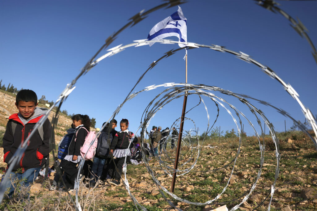Palestinian children passing razor wire erected by Israeli settlersblocking their path to school in the West Bank, on April 14, 2026. Source: Hazem Bader/AFP via Getty Images.