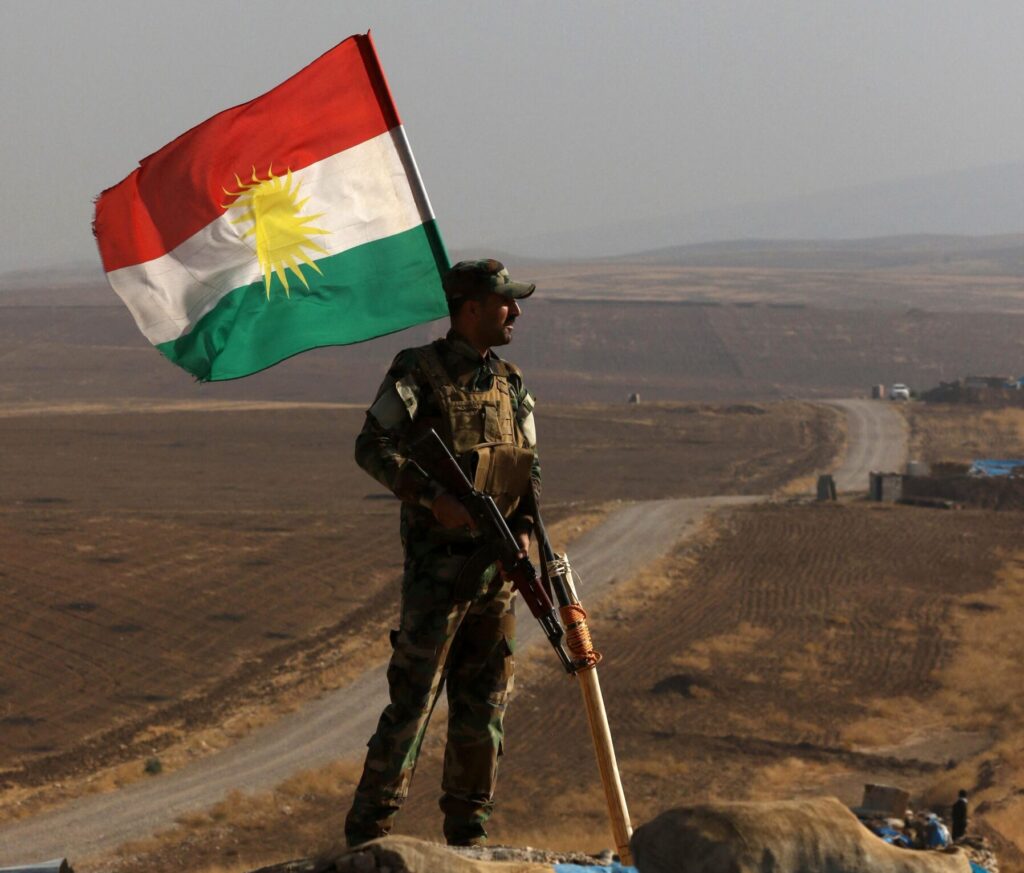 An Iraqi Kurdish Peshmerga fighter, next to a Kurdish flag, holds a position in Sheikh Ali village north of Mosul. Source: Safin Hamid/AFP via Getty Images.