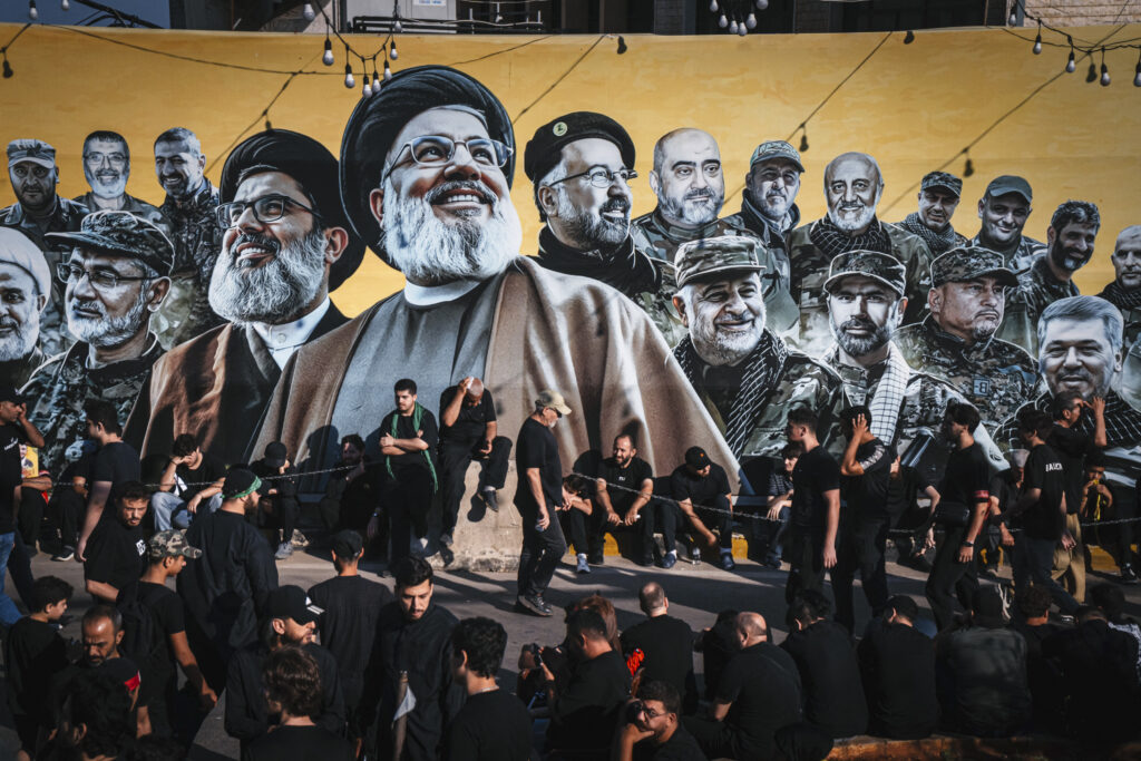 Men sit and stand near a large mural, featuring Hassan Nasrallah and other Hizballah members, during a mourning procession in the southern suburbs of Beirut on June 26, 2026. Photo by Nael Chahine/Middle East Images/AFP via Getty Images.