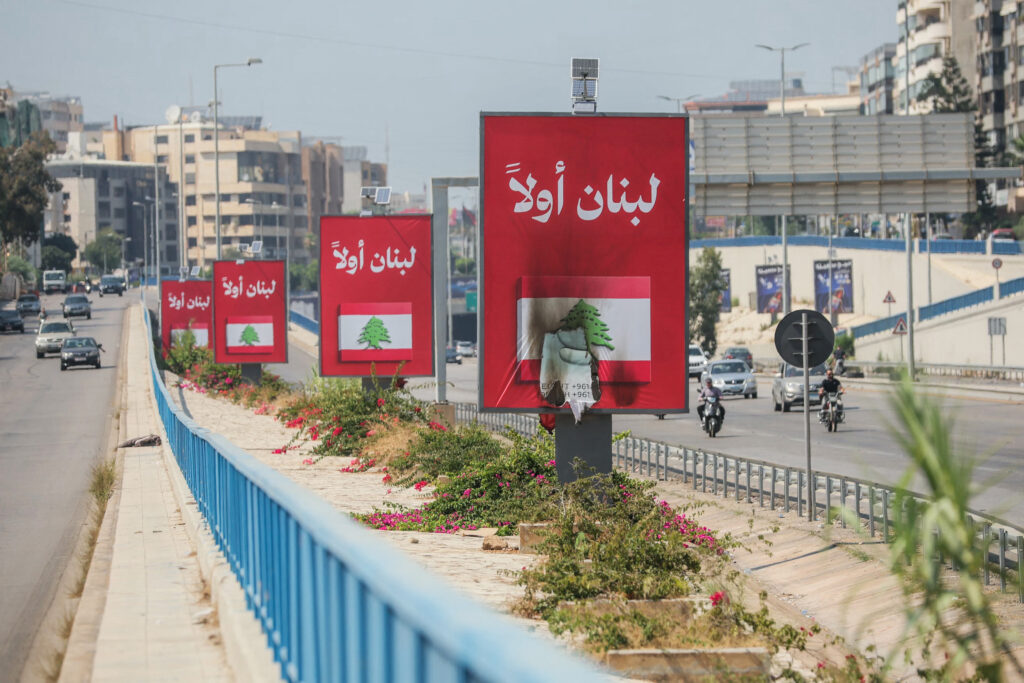 Vehicles drive past billboards that read, in Arabic, "Lebanon first," one of which has been set on fire, along Beirut's airport road near Tehran-backed Hizballah's stronghold, amidst tensions following the Lebanon-Israel agreement on June 28, 2026. Photo by Ibrahim AMRO/AFP via Getty Images.