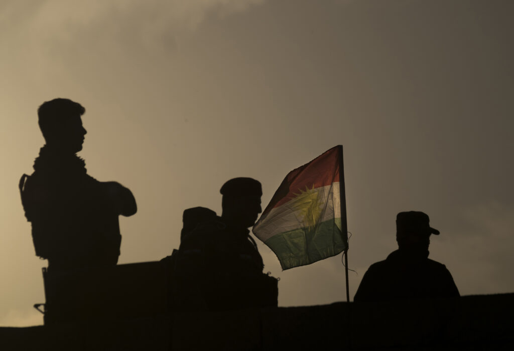 Iraqi Kurdish Peshmerga fighters stand next to a Kurdish flag near the city of Bashiqa, in the Ninawa Governorate east of Mosul, on November 6, 2016. Source: Morteza Nikoubazl/NurPhoto via Getty Images.